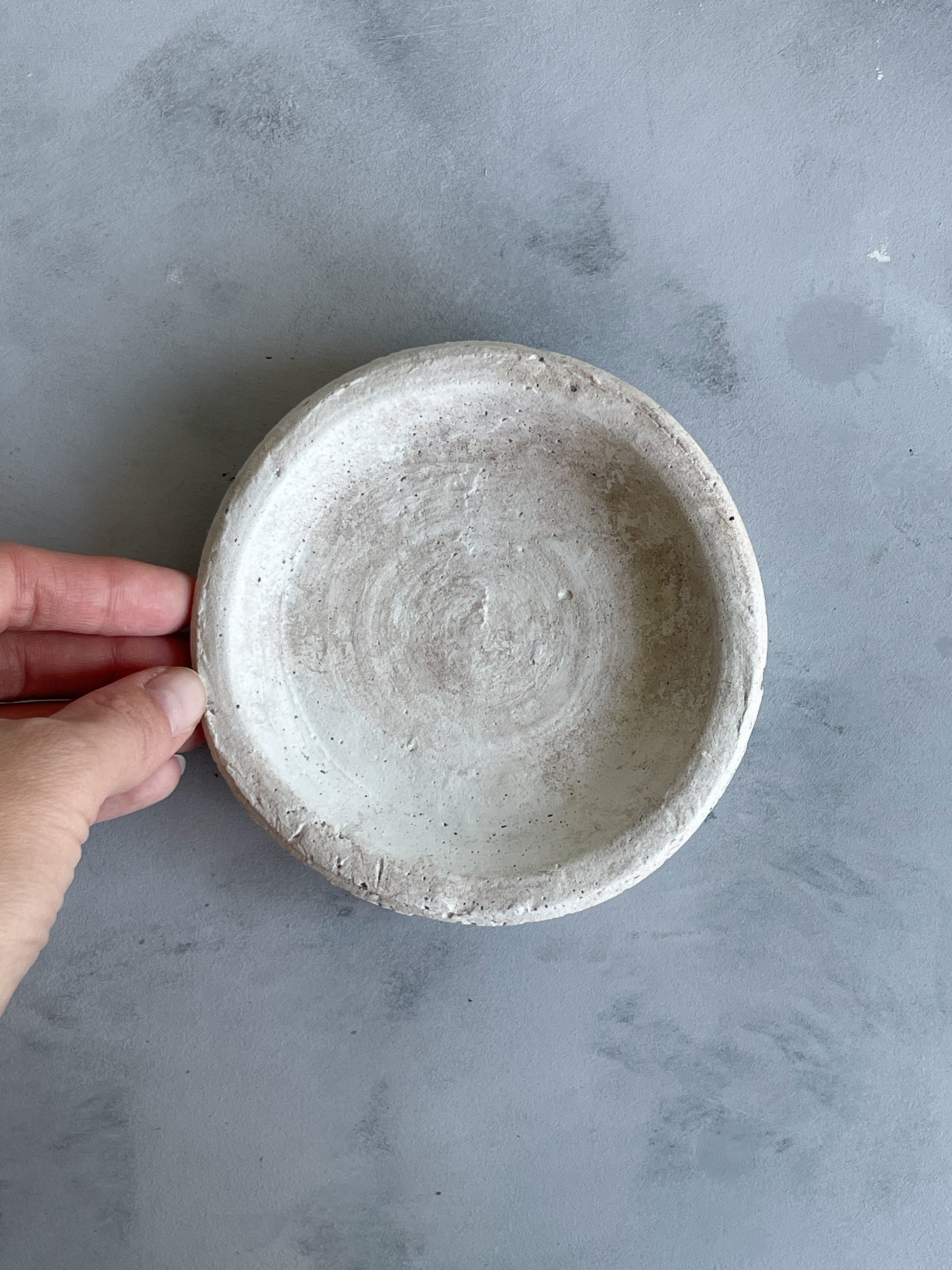 Top-down view of the handmade cement dish from the Milos Collection, featuring a smooth, rounded shape in light off-white tones.